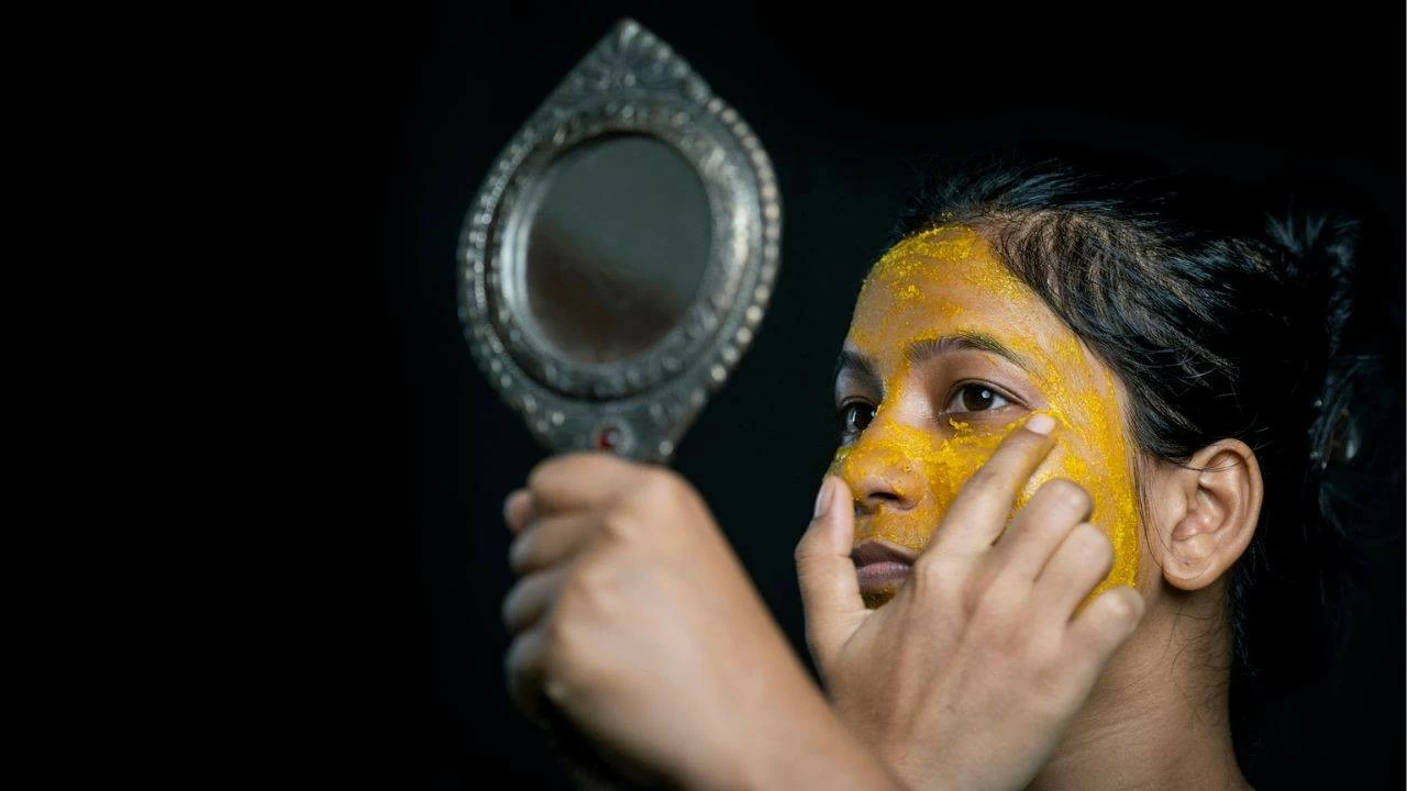A young woman applies turmeric face mask for achieving glowing skin.