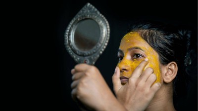 A young woman applies turmeric face mask for achieving glowing skin.