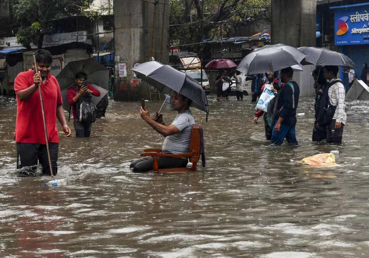 In a bizarre move, a man placed a chair in the middle of a waterlogged road and sat there with an umbrella amid rainfall in Mumbai on Tuesday. (PTI) 