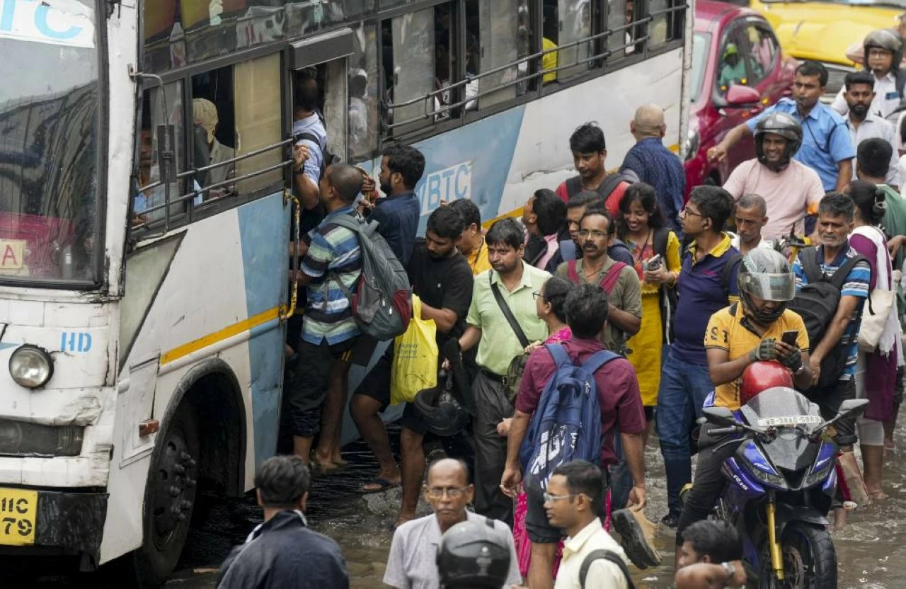 Commuters board a bus on a waterlogged road after rain lashes Kolkata
