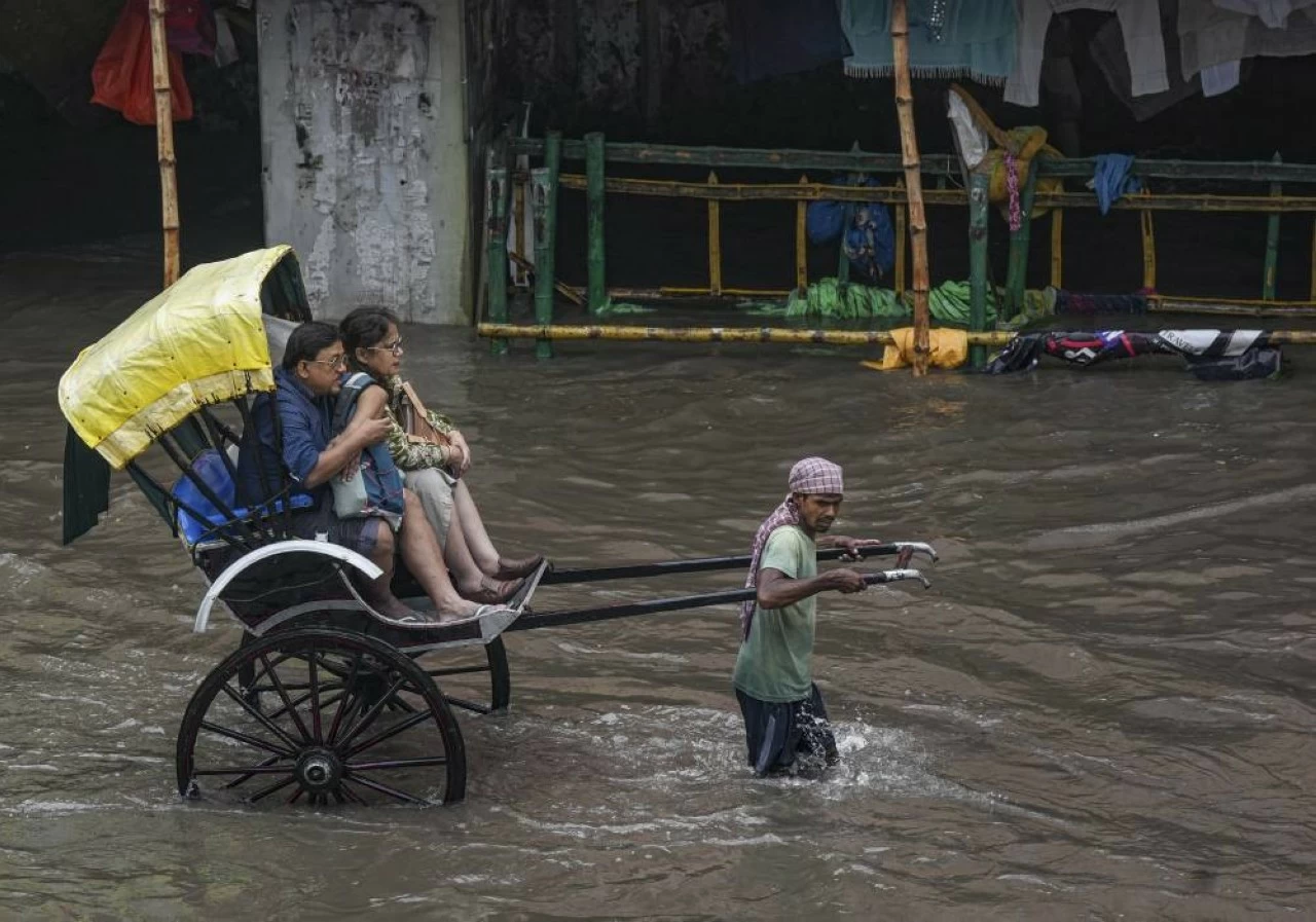 A rickshaw puller carries passengers through a waterlogged road following rain, in Kolkata
