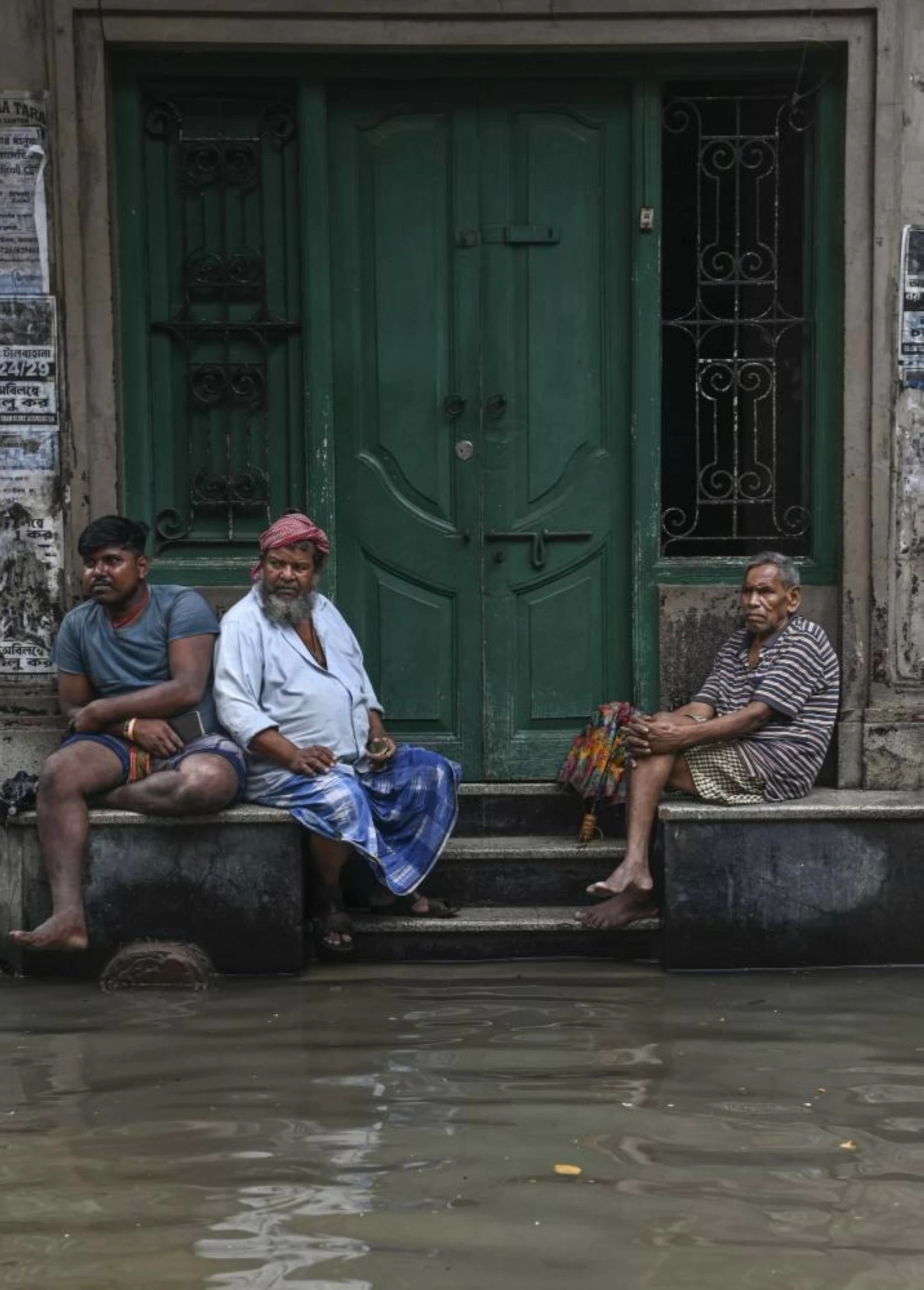 People sit on a raised platform outside a house at a waterlogged locality following rain, in Kolkata