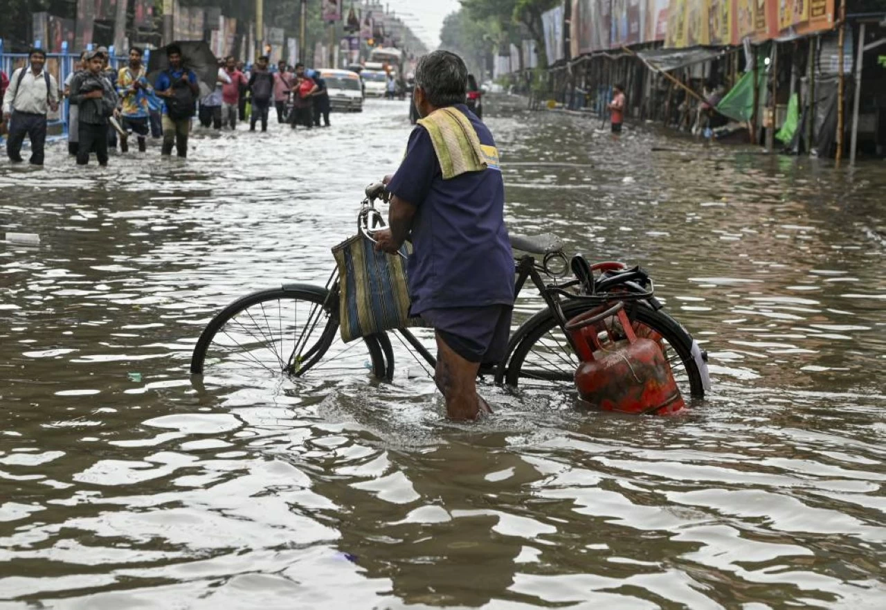 A delivery man carrying LPG cylinders on a bicycle wades through a flooded road after heavy rainfall
