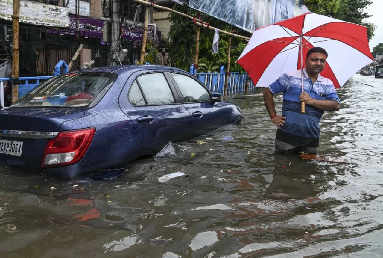  A man walks past a partially submerged car on a flooded road after heavy rainfall