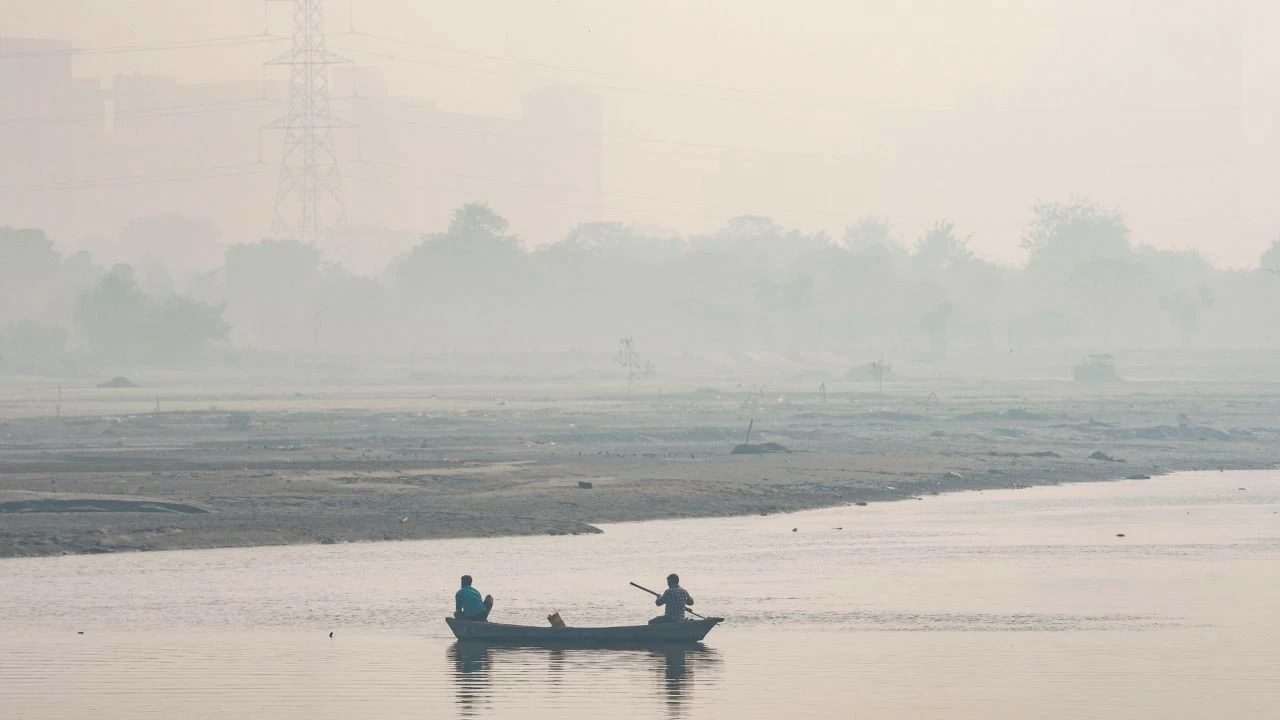 Men row a boat in the Yamuna river as a layer of smog engulfs the city amid deterioration in the air quality, in New Delhi