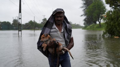 A man carrying a dog walks along a flooded street, following heavy rainfall in Wellampitiya. (Photo credit: Reuters)