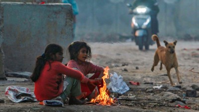 Children warm themselves around a small bonfire on a winter morning, near Sarai Kale Khan area