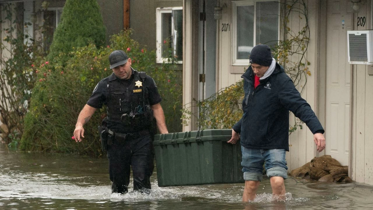 Deputy Sheriff Kalani Apilado helps Brandon Phasith carry belongings while evacuating amidst rising floodwater, as an atmospheric river brings rain and flooding to the Pacific Northwest, in Sultan, Washington
