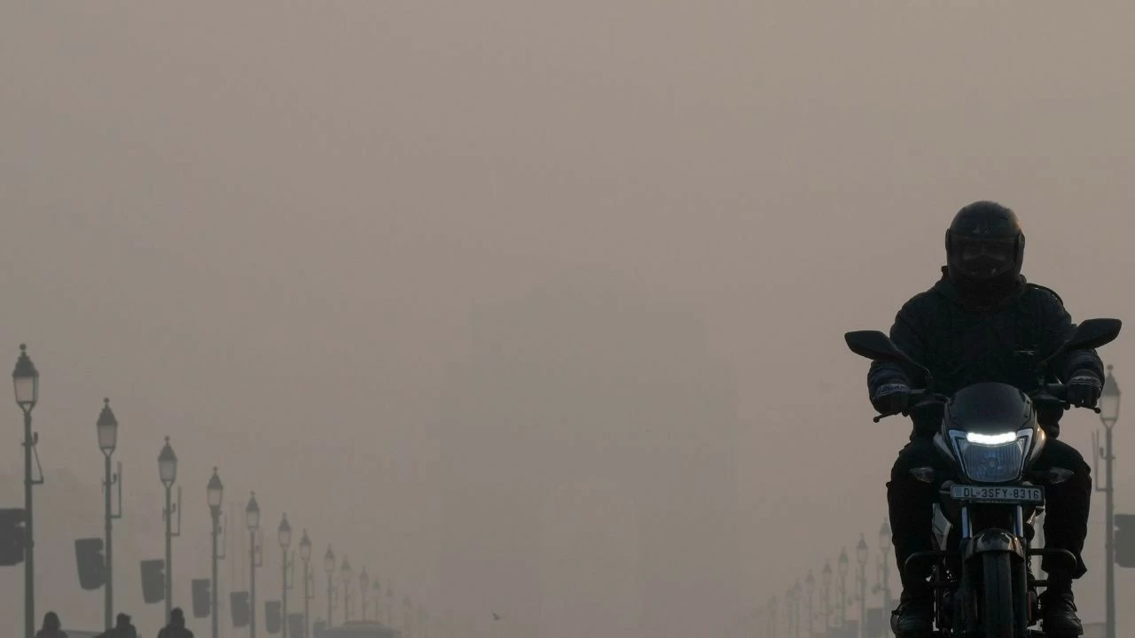 A commuter rides a two-wheeler on the Kartavya Path in the backdrop of the India Gate shrouded in smog on a winter morning, in New Delhi