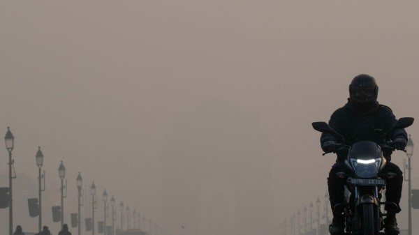 A commuter rides a two-wheeler on the Kartavya Path in the backdrop of the India Gate shrouded in smog on a winter morning, in New Delhi