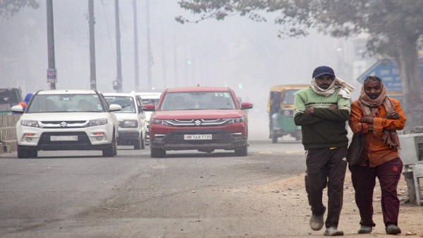 People walk along the roadside amid low air quality on a winter morning, in Gurugram, Sunday, Dec. 21, 2025. (PTI Photo)