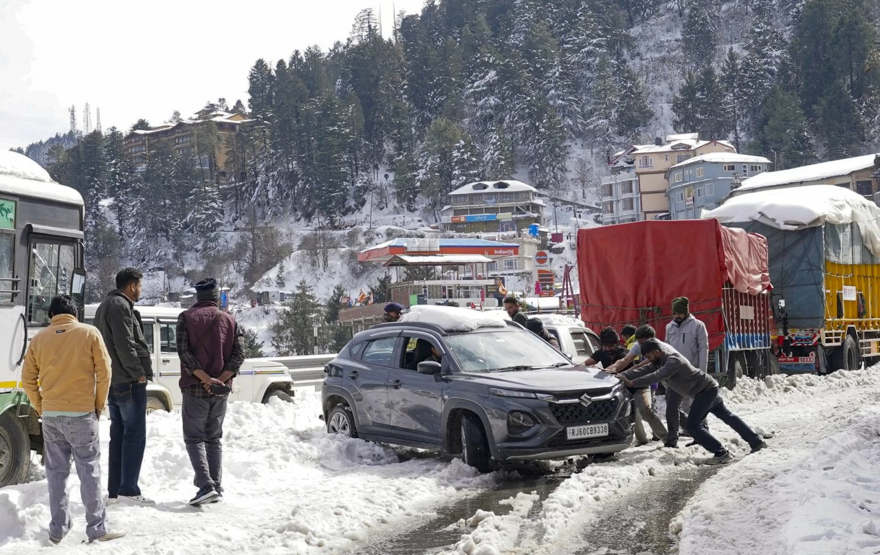 People try to push a car that stalled on a snow-covered road after snowfall in Shimla, Himachal Pradesh